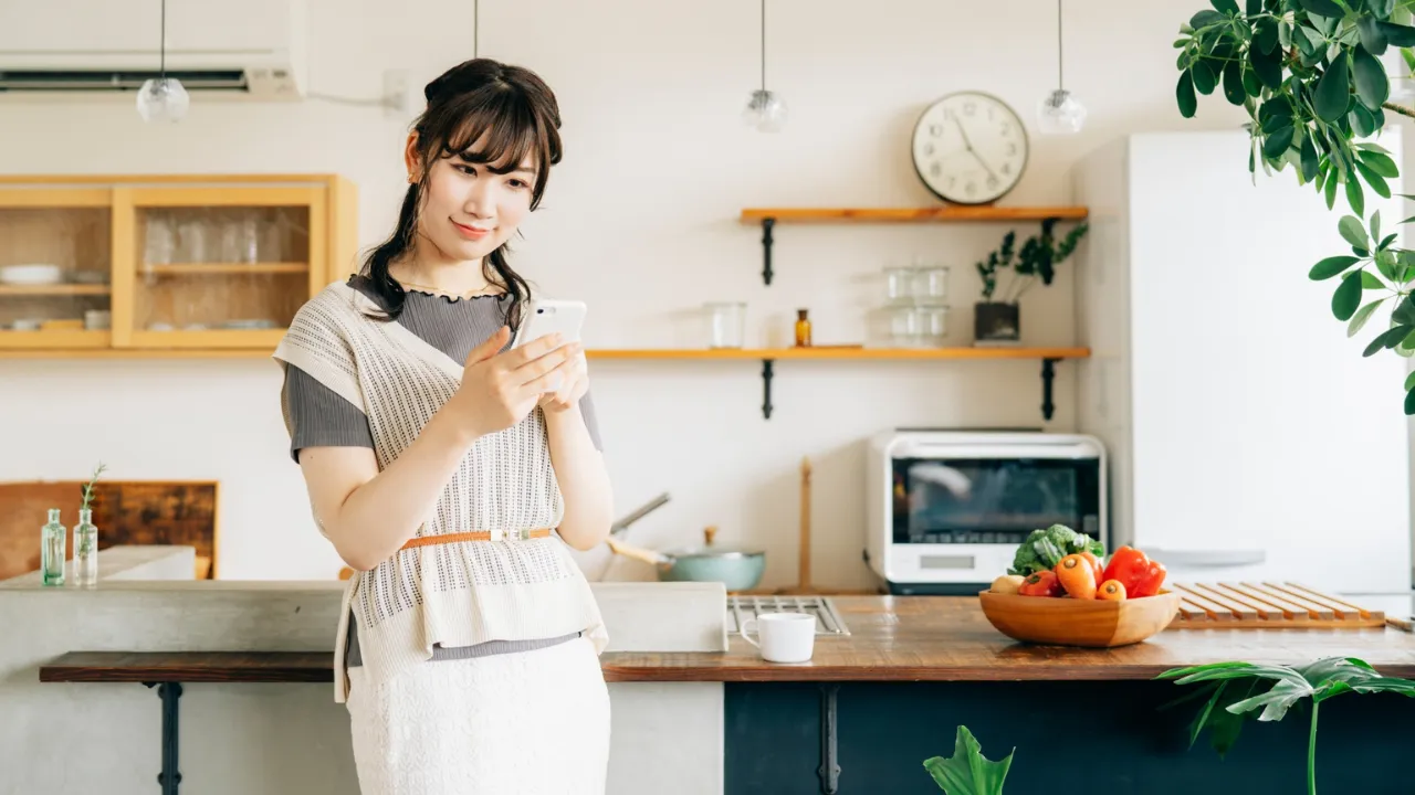 キッチンで家計簿アプリを操作する若い女性