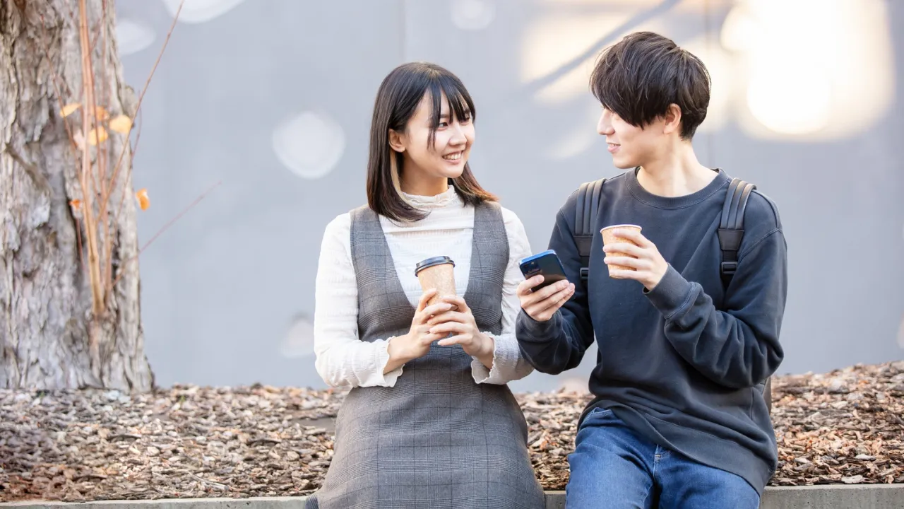 外でコーヒーを飲みながら会話する若いカップル
