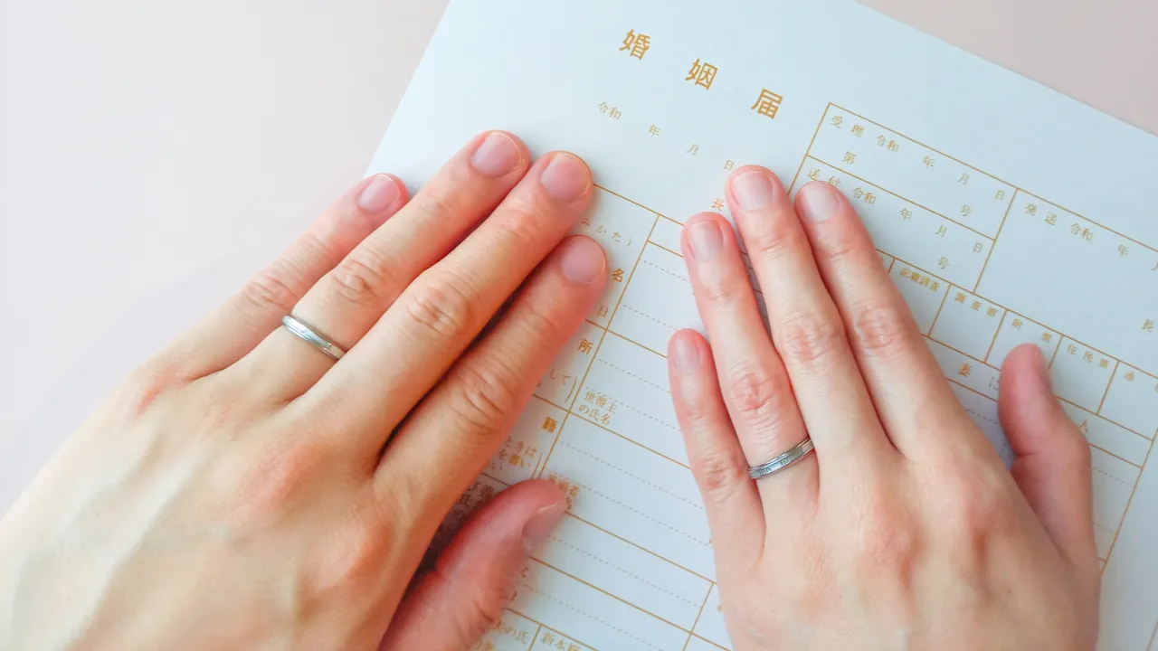 婚姻届の上に並んだ結婚指輪をした二人の手